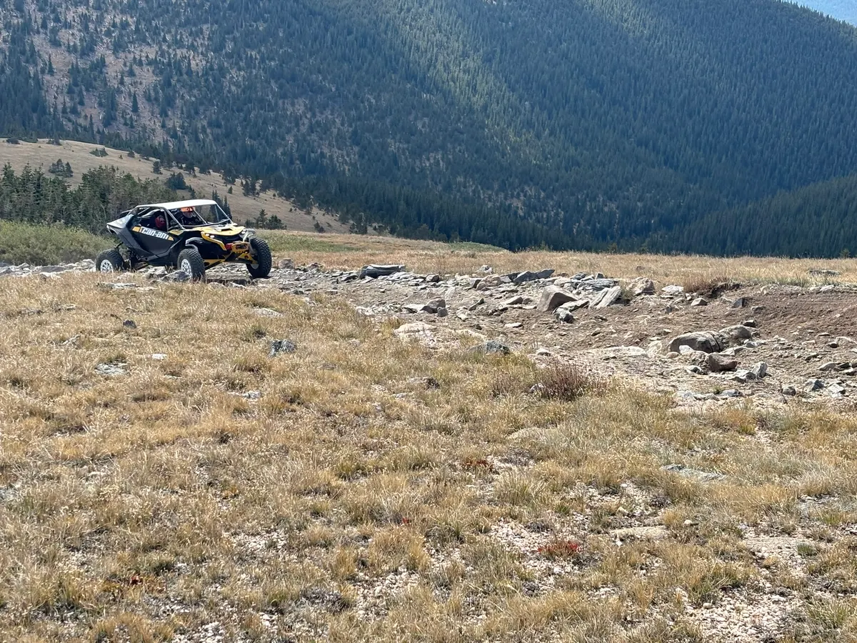 A yellow and black Can-Am on a rocky alpine trail above the treeline