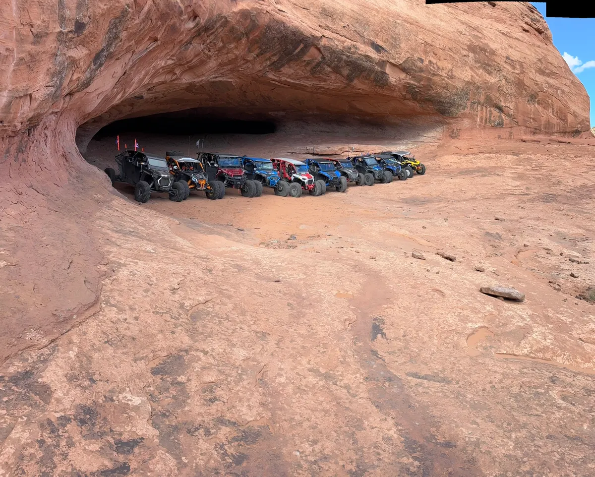 A line of side-by-sides parked under a sandstone arch