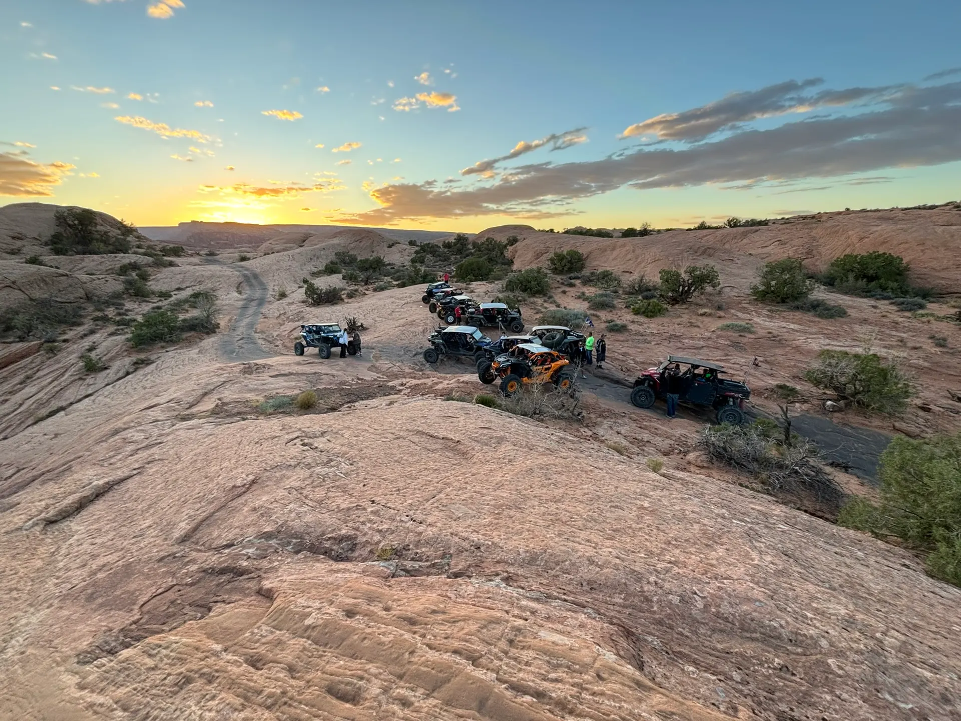 A group of side-by-sides parked on slickrock at sunset