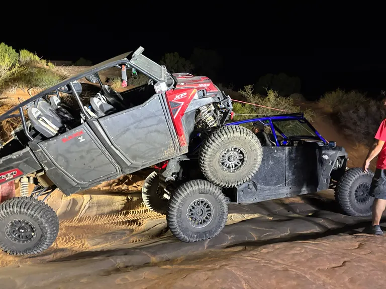 A Polaris RZR being winched upright on slickrock at night