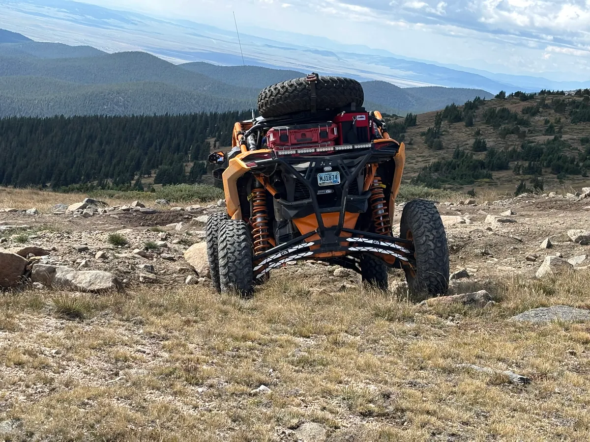 An orange Can-Am with a spare tyre and toolbox parked at a mountain overlook