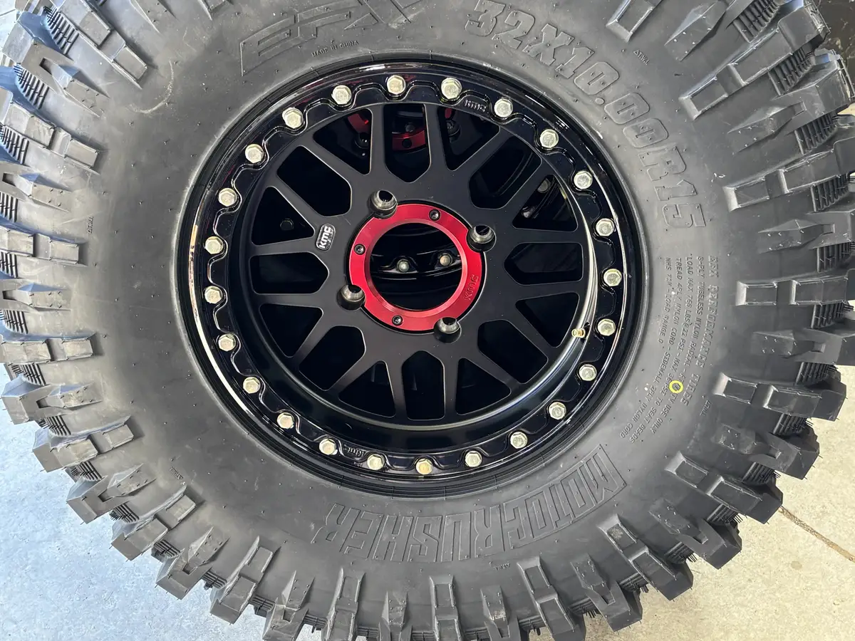 Close-up of a black beadlock wheel with a red center ring and bolted bead ring on a new off-road tire