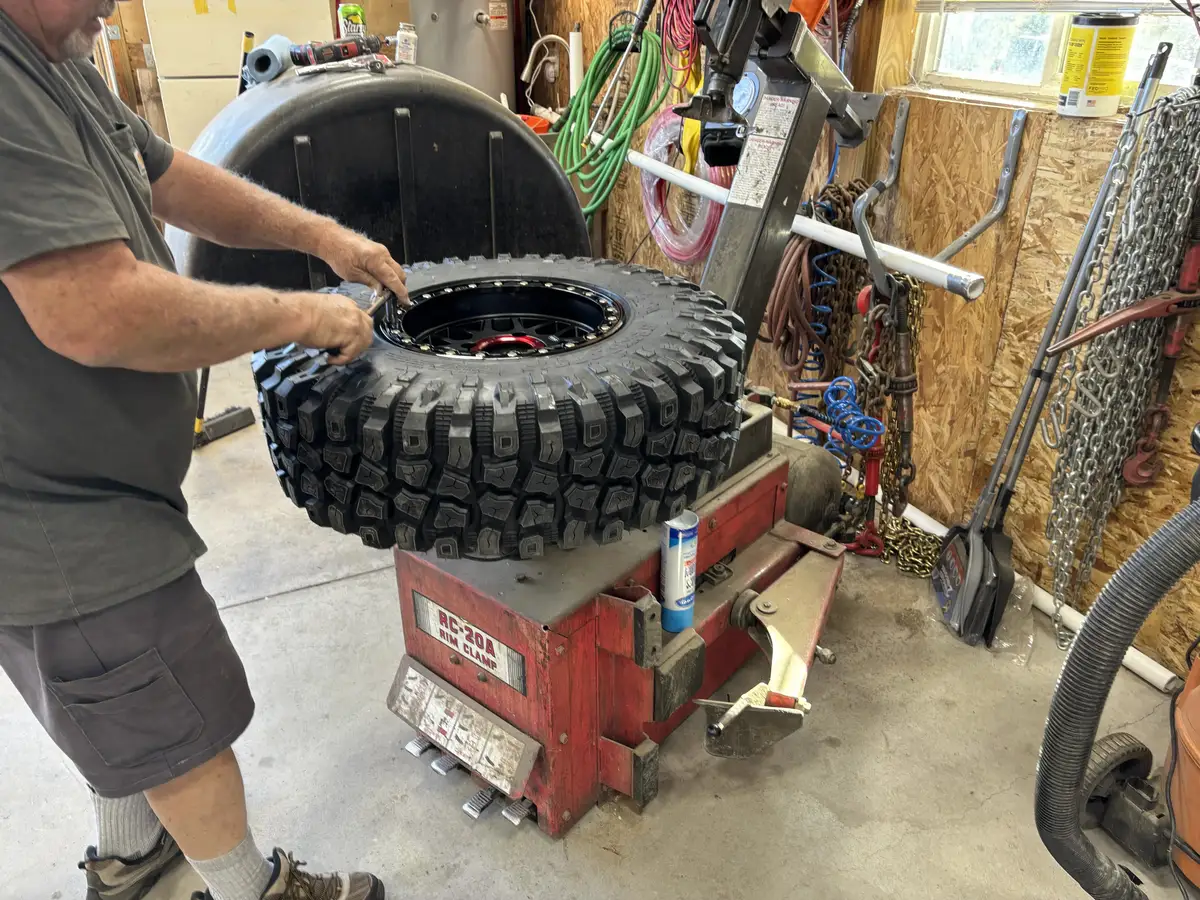 A technician working a large off-road tire onto a black beadlock wheel at the shop's tire machine