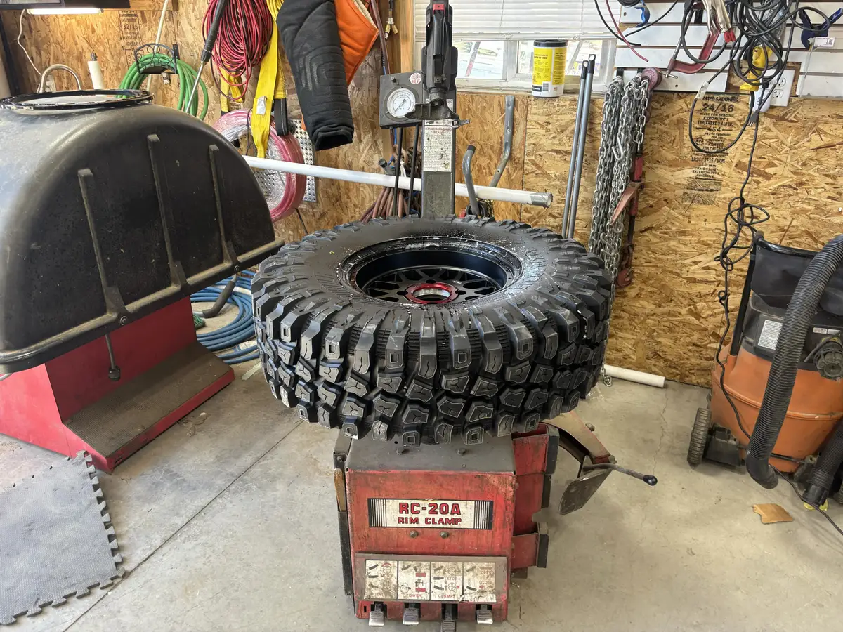 A freshly mounted off-road tire on a black beadlock wheel sitting on the tire machine in the shop bay