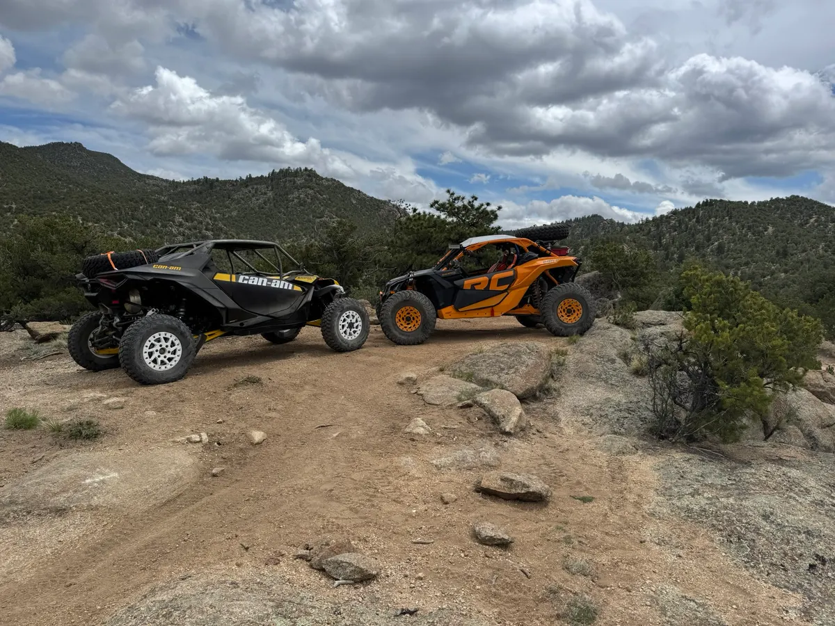 A black Can-Am and an orange Can-Am parked on a ridge in the pines